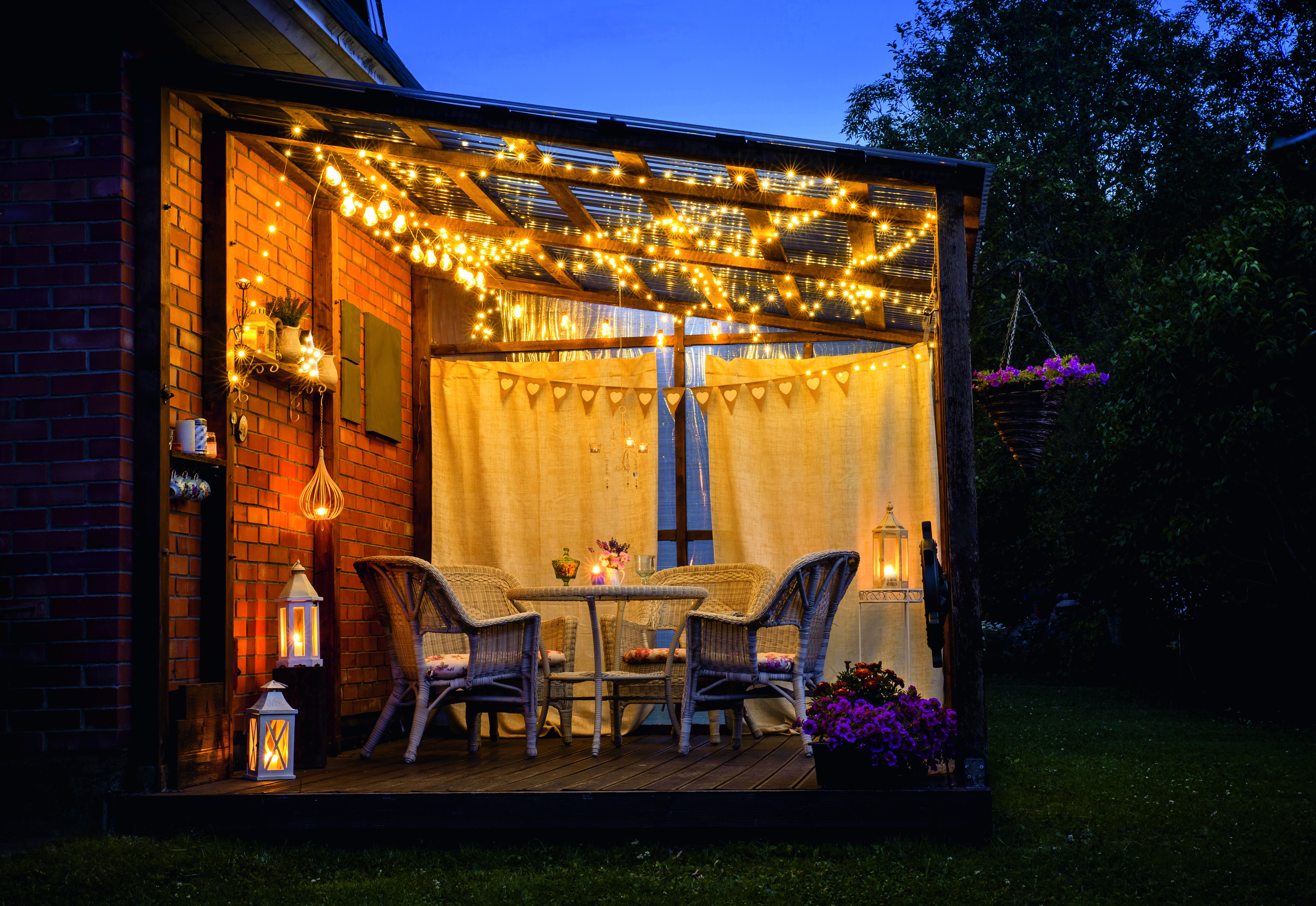 Gartenmöbel unter einem Holzpavillon bei Nacht, beleuchtet durch Lichterketten.