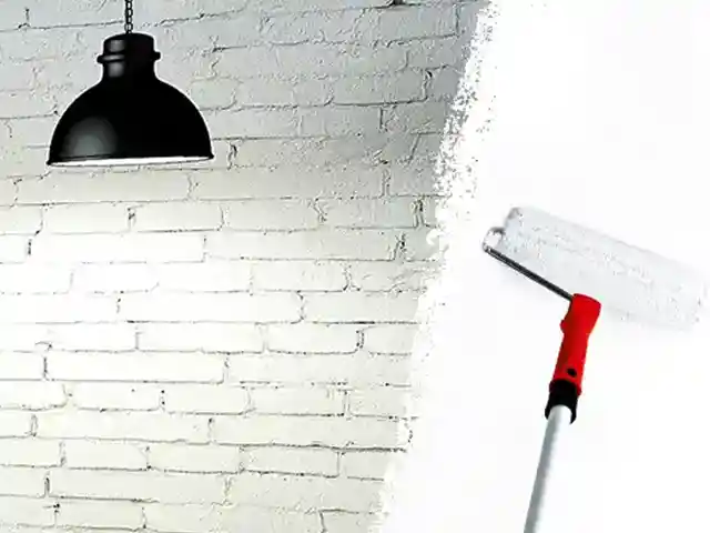 Eine Farbrolle malt eine weiße Ziegelwand an; eine Lampe hängt über der Szenerie.