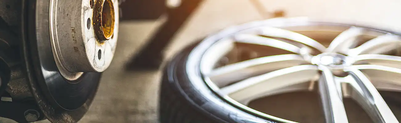 Ein abgenommenes Autoreifenrad lehnt neben einer Bremsscheibe in einer Werkstattumgebung.