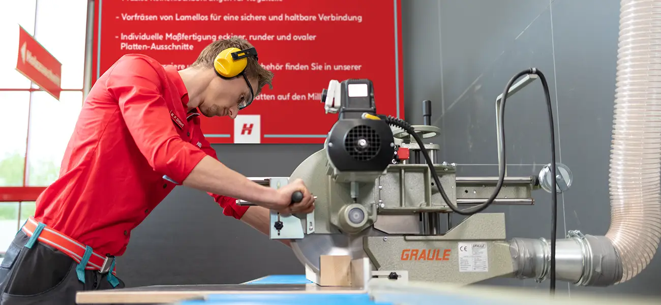 Ein Hellweg Mitarbeiter schneidet in einer Werkstatt Holz zu.