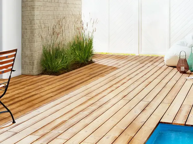 Ein Holzdeck umgibt einen Pool, neben einer Backsteinmauer mit grasähnlichen Pflanzen.