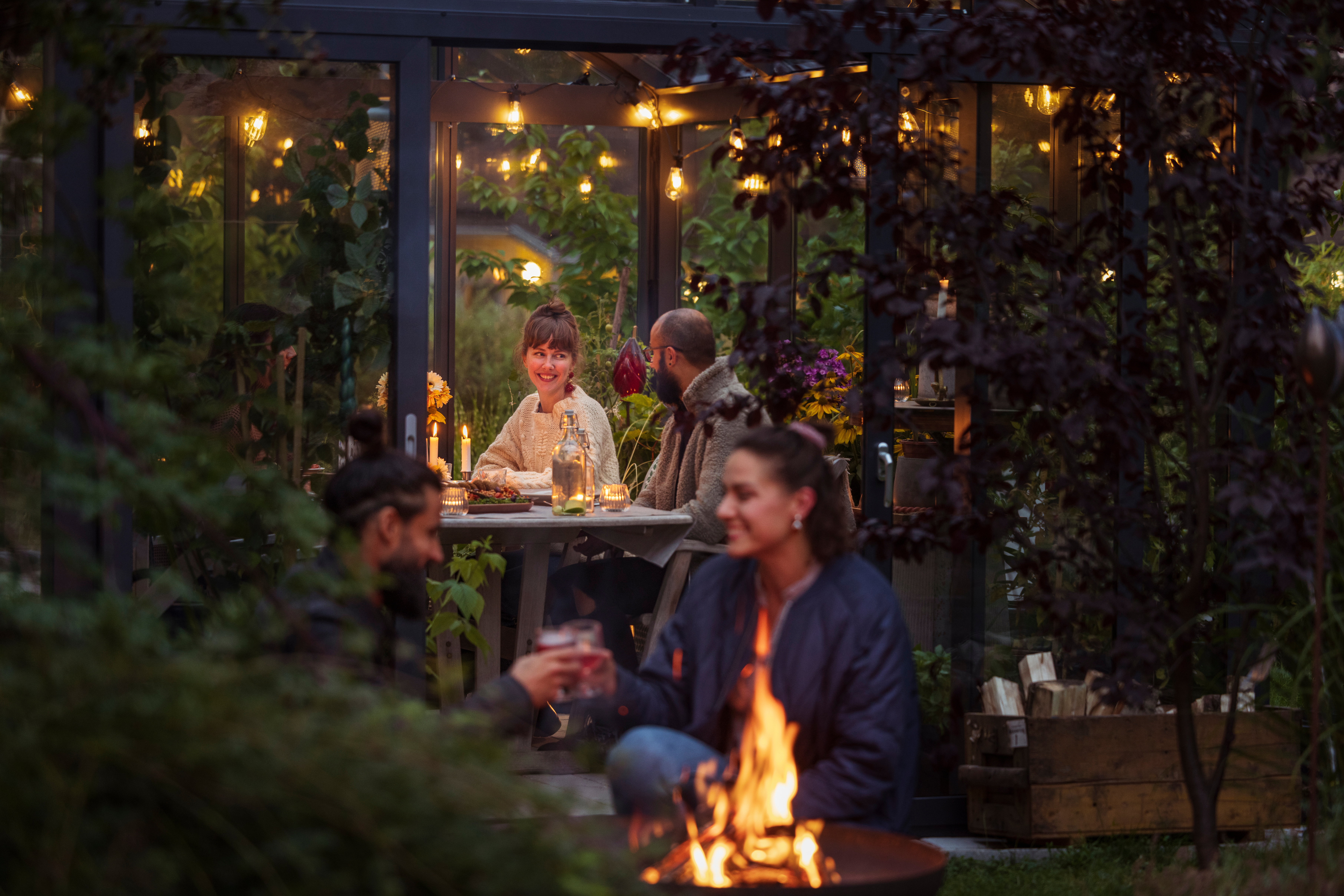 Menschen genießen ein Abendessen und ein Feuer in einem gemütlichen Gartenpavillon.