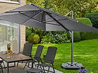 Ein großer Sonnenschirm spendet Schatten über einem Terrassentisch mit Stühlen im grünen Garten.