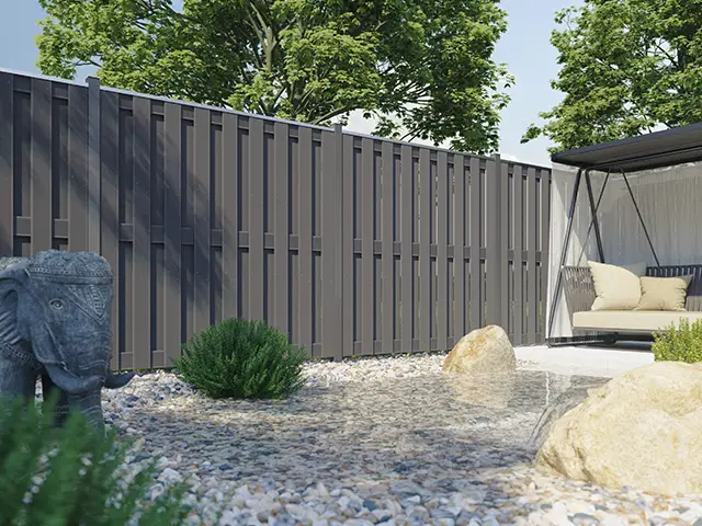 Ein Elefant aus Stein steht neben einem modernen Zaun in einem steinigen Garten.