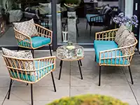 Rattanmöbel mit blauen Kissen umgeben einen kleinen Tisch auf einer Terrasse.