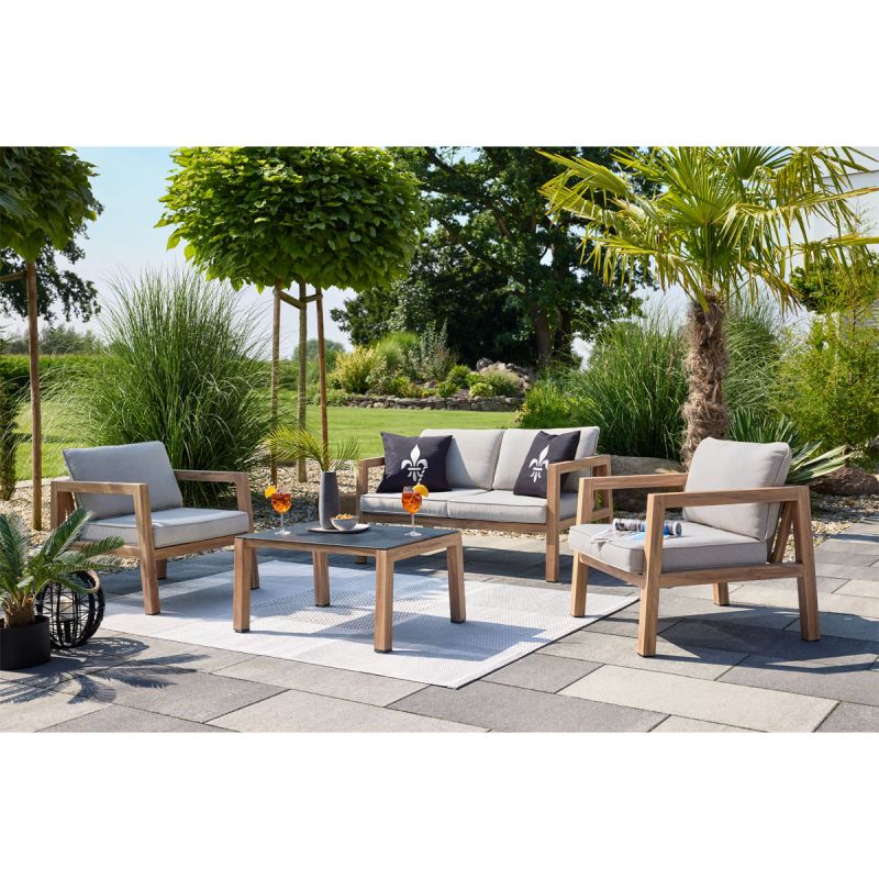 Eine Gartenmöbel-Sitzgruppe mit Sesseln und Tisch steht auf einer Terrasse, umgeben von Pflanzen.