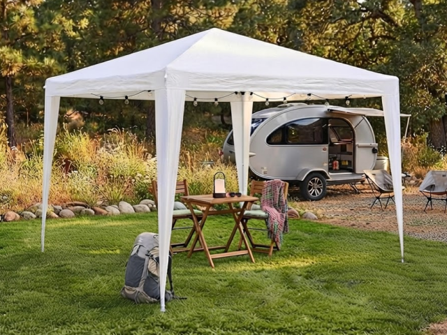 Pavillon auf Wiese am Waldrand mit kleinem Campingwagen und Klapptisch aus Holz
