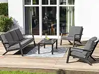 Eine Gartenmöbelgruppe aus Sofa, Stühlen und Tisch steht auf einer Holzterrasse vor Fenstern.