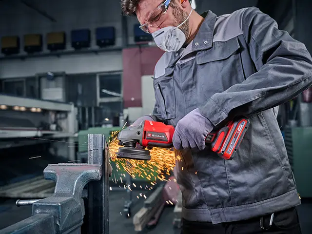 Ein Mann schleift in einer Werkstatt mit einem Winkelschleifer von Einhell ein Metallstück.