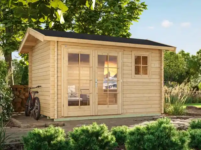 Ein Holzschuppen steht im Garten, umgeben von Bäumen und einem Fahrrad links daneben.