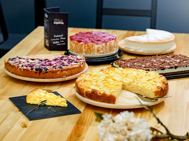 Mehrere Kuchen stehen auf einem Holztisch im Café Augsburg.