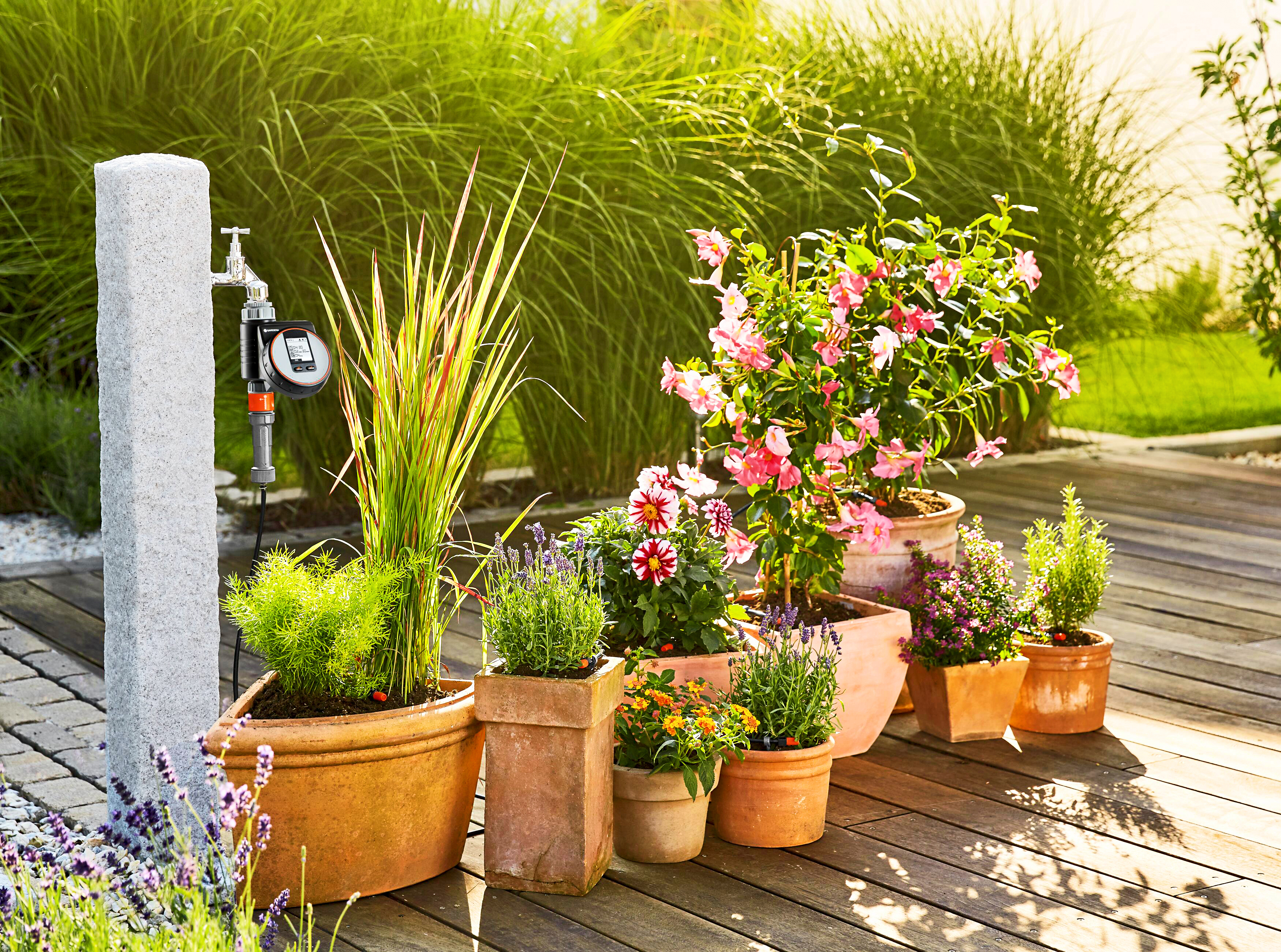 Ein Bewässerungscomputer angeschlossen am Wasserhahn neben mehreren Blumenkübeln