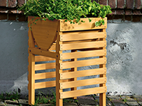 Ein hölzernes Hochbeet, gefüllt mit grünen Pflanzen, steht vor einer Mauer.