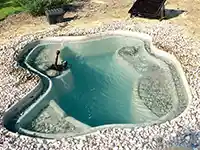 Ein kleiner Teich mit Wasserpumpe, umgeben von Kieselsteinen, befindet sich im Freien.