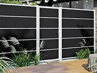 Ein hoher schwarzer Zaun steht vor Pflanzen auf einer Holzterrasse.