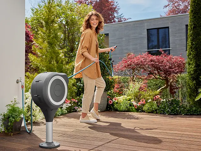 Eine Frau bewässert ihre Gartenpflanzen mit einem Gartenschlauch von Gardena.