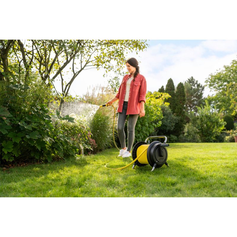 Eine Frau die Blumen gießt mit einem Schlauchwagen