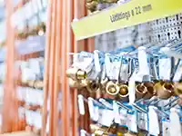 Metallbeschläge hängen neben Kupferrohren in einem Baumarktregal.