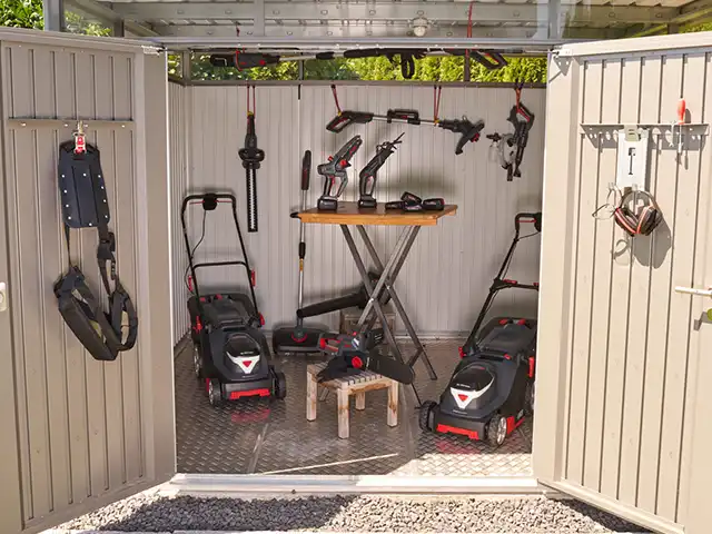 Werkzeuge hängen und stehen ordentlich in einem offenen Schuppen mit grauen Wänden und Boden.