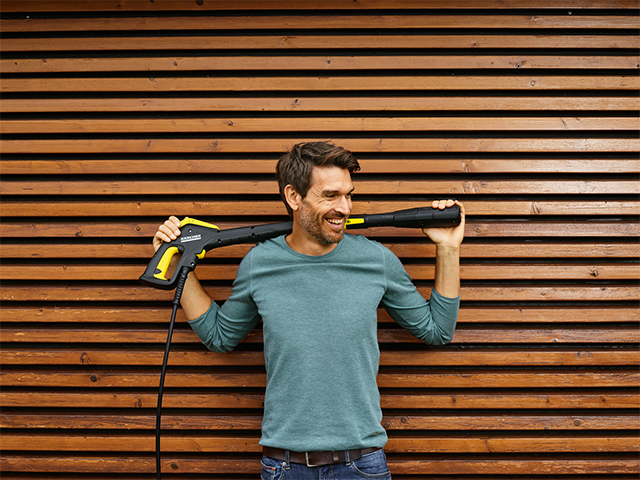 Mann mit Kärcher Elektrogerät vor einer Holzwand