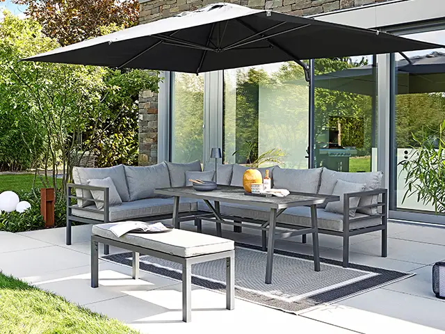 Eine Gartensitzgruppe mit Sonnenschirm steht auf einer Terrasse vor einem modernen Haus.