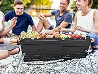 Eine Gruppe von Freunden sitzt um einen mobilen Grill im Freien.