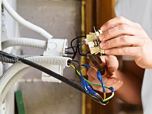 Eine Person repariert Kabel mit einer Zange in einem häuslichen Elektroinstallationsbereich.