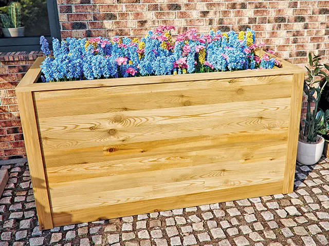 Ein Hochbeet mit bunten blühenden Blumen steht neben einer Backsteinmauer.