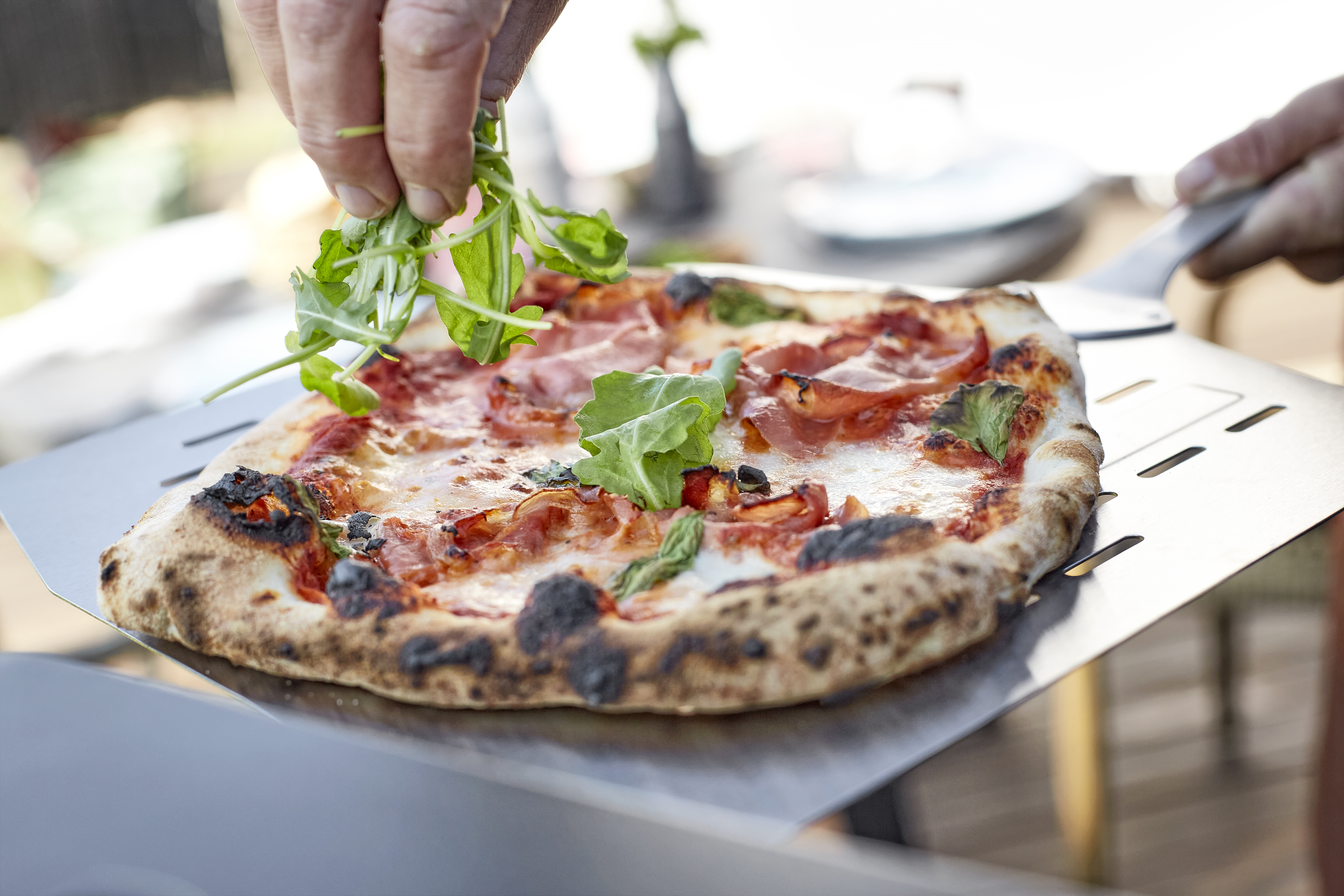 Eine Pizza die gerade mit frischem Salat belegt wird