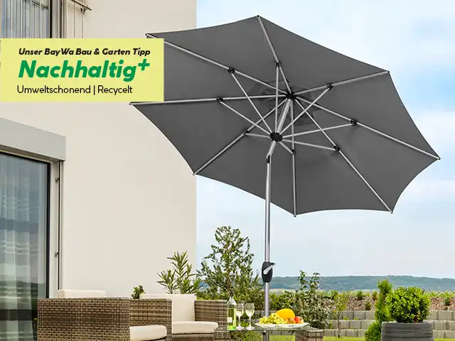 Ein großer, grauer Sonnenschirm steht geöffnet auf einer Terrasse neben einem Gartenmöbel-Set.