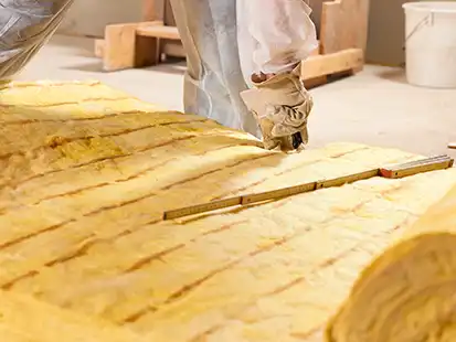 Eine Person schneidet Glaswolle mit einem Messer in einer Werkstattumgebung.