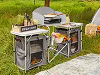 Eine Campingküche mit Grill und Utensilien steht auf einer Wiese.