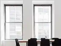 Ein Konferenztisch mit schwarzen Stühlen steht in einem Raum mit zwei großen Fenstern.