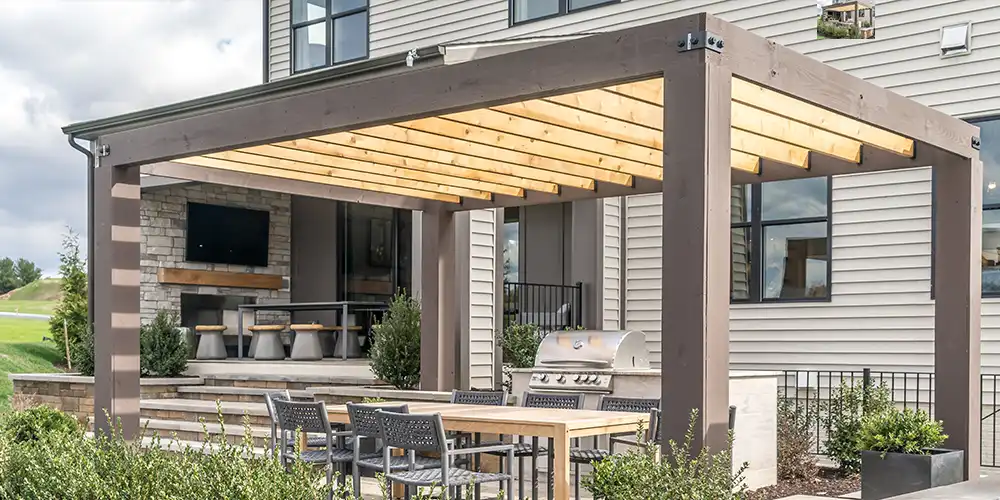 Eine Pergola bedeckt einen Essbereich im Freien neben einem modernen Haus mit Grillplatz.