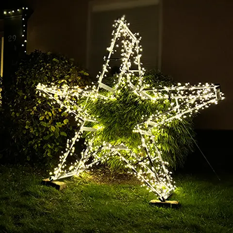 Ein beleuchteter Stern aus Klappböcken leuchtet nachts im Garten vor einem Haus.