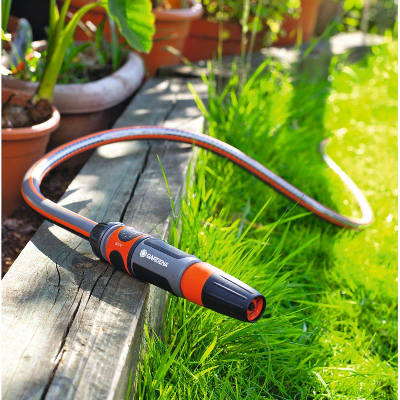 Ein Gardena Gartenschlauch mit Düse liegt auf einem Holzbrett neben grünen Pflanzen.