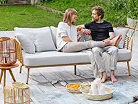 Zwei Personen sitzen auf einem Sofa und unterhalten sich, umgeben von Gartenmöbeln im Freien.