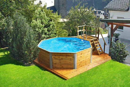 Ein achteckiger Pool auf einer Holzplattform befindet sich in einem grünen, von Bäumen umgebenen Garten.
