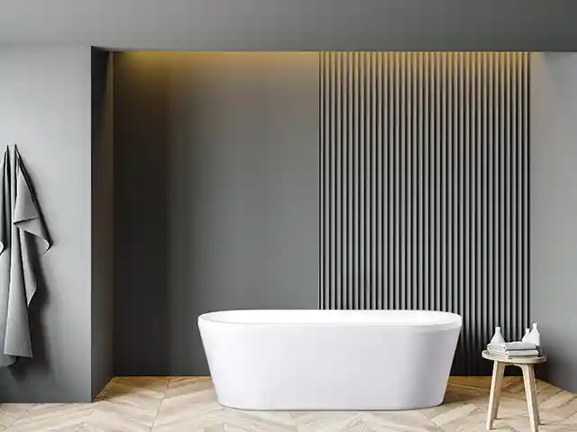 Eine weiße Badewanne steht vor einer dunkelgrauen Wand mit vertikalen Streifen, daneben Handtücher.