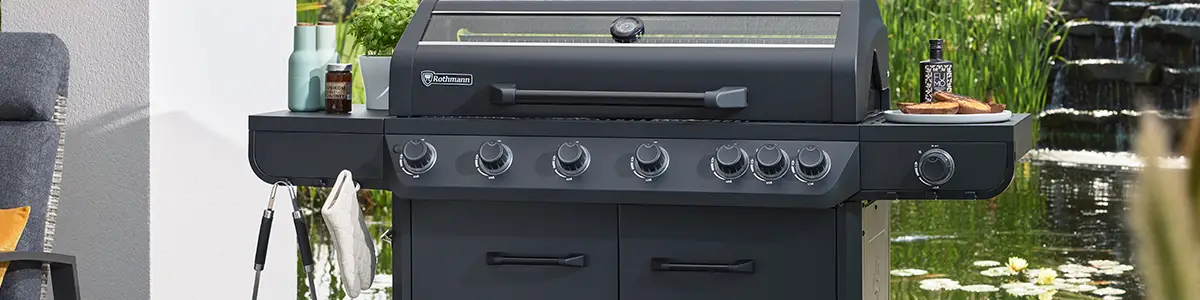 Ein großer Rothmann Grill mit mehreren Knöpfen steht auf einer Terrasse vor einem Teich.