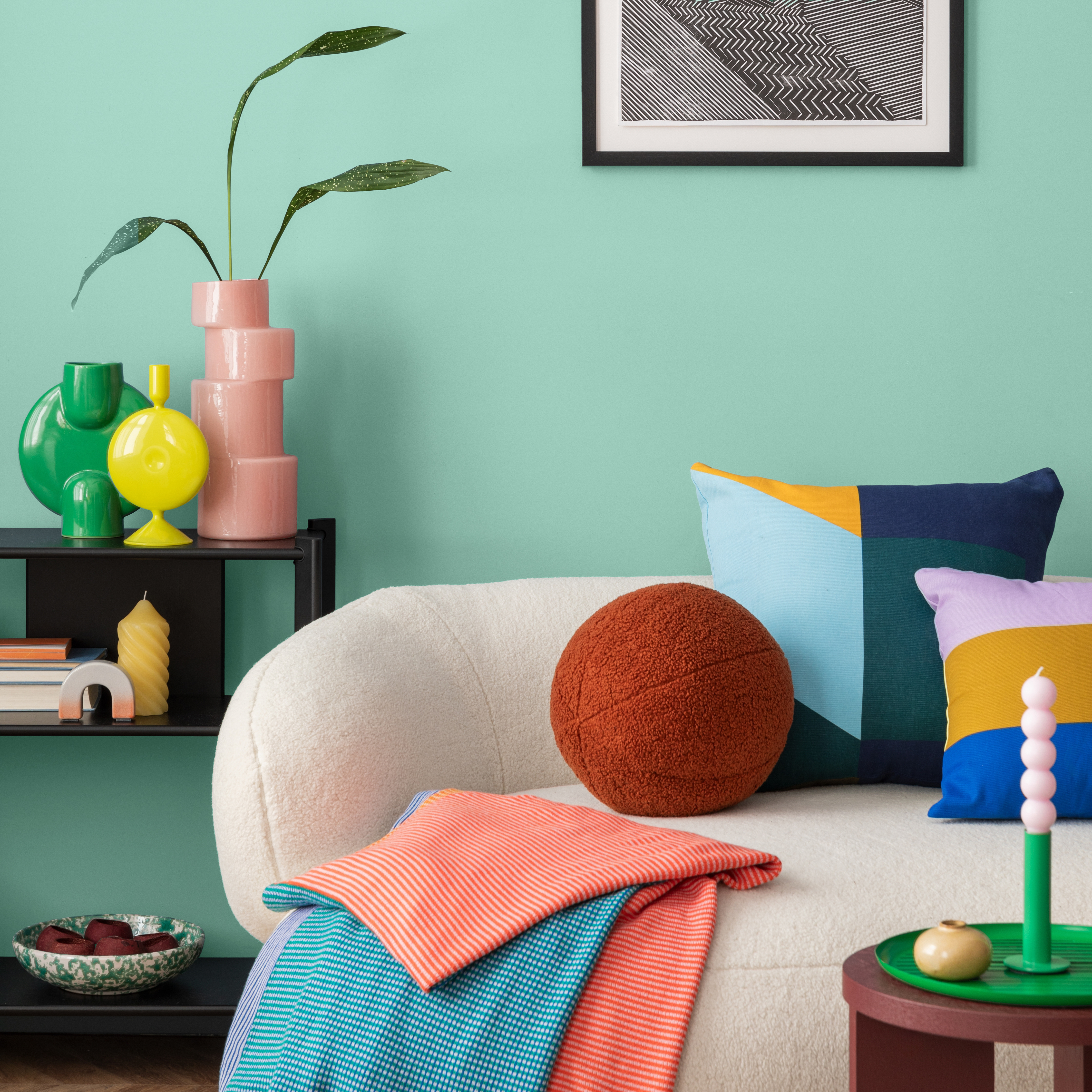 Mintfarbener Hintergrund mit heller Couch und buntgemusterten Decken und Kissen