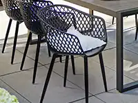 An einem schwarzen Tisch steht ein schwarzer Stuhl leicht herausgezogen.