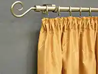 Ein goldener Vorhang hängt an einer verzierten Stange vor einer grauen Wand.