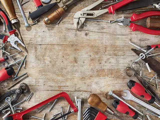 Werkzeuge wie Zangen und Schraubenschlüssel liegen auf einem hölzernen Arbeitstisch verteilt.