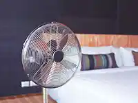 Ein Ventilator dreht sich in einem Schlafzimmer neben einem Bett mit bunten Kissen.