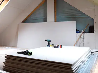 Ein Stapel Gipskartonplatten liegt mit Werkzeugen darauf in einem ausgebauten Dachgeschoss.