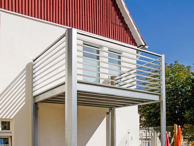 Ein Balkon mit Metallgeländer ragt aus einem hellen Gebäude unter klarem, blauem Himmel hervor.