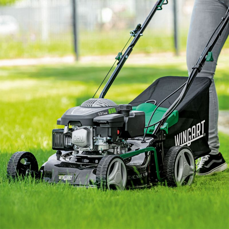 Ein Rasenmäher, betrieben von einer Person, schneidet das Gras auf einer grünen Wiese.