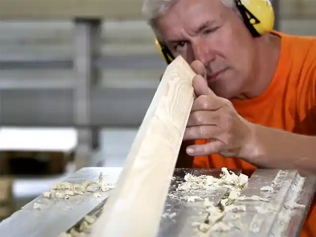 Ein Mann glättet ein Holzbrett mit einer Hobelmaschine in einer Werkstatt.
