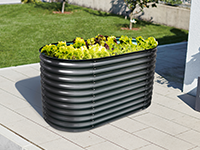 Ein Hochbeet mit grünen Pflanzen steht auf einer gefliesten Terrasse im Garten.